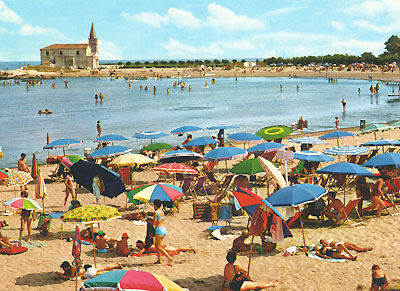 Caorle-Postkarte von 1960. Strand mit vielen Menschen und bunten Sonnenschirmen.
