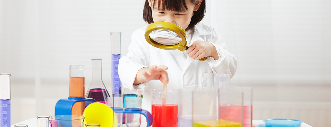 Kleines Mädchen im weißen Laborkittel mit Lupe in der Hand