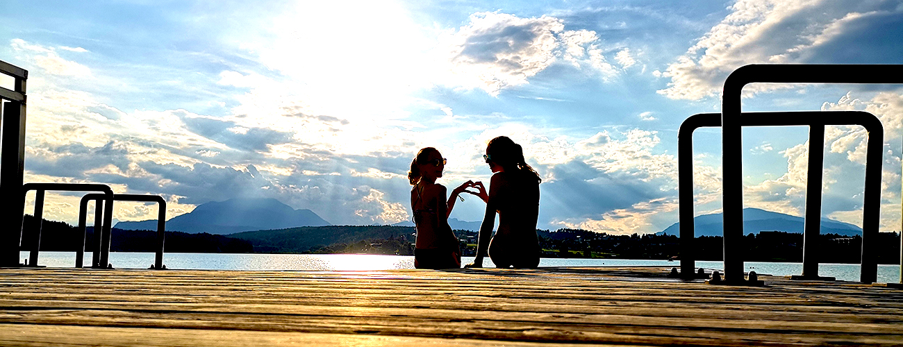 Zwei junge Frauen sitzen im Sonnenuntergang am Steg.