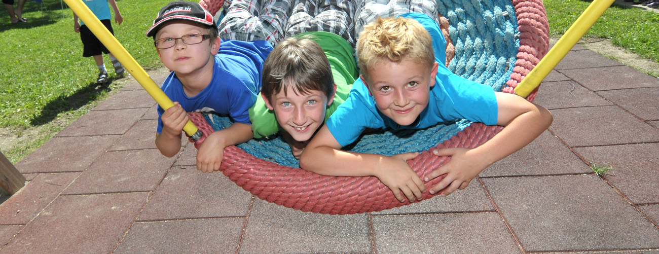 Drei Jungs in Sommerbekleidung schaukeln in Nestschaukel im Garten